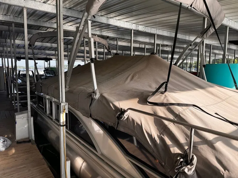 Slide: The Image of A 2023 Bennington 23SXSB pontoon boat is docked under a covered area, with a protective cover on. - 12