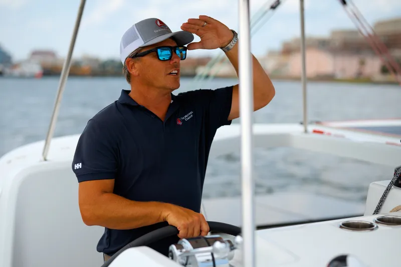 Slide: The Image of Man steering 2026 Lagoon 38 catamaran, wearing sunglasses and cap, on a sunny day. - 133