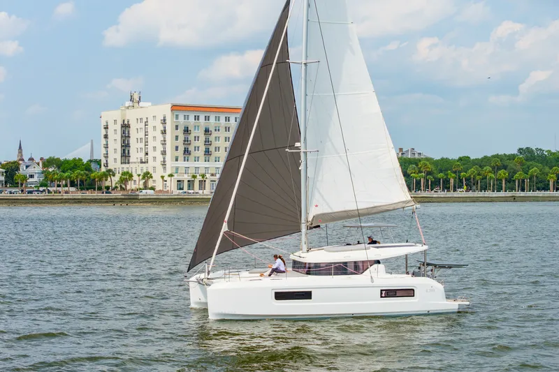 Slide: The Image of 2026 Lagoon 38 catamaran sailing near a coastal city with palm trees and buildings. - 104
