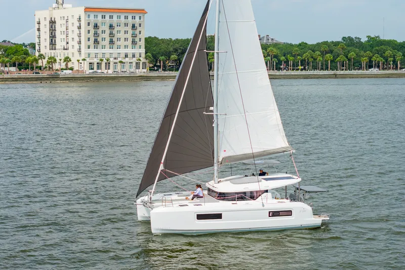 Slide: The Image of 2026 Lagoon 38 catamaran sailing near a coastal city with palm trees and buildings. - 99