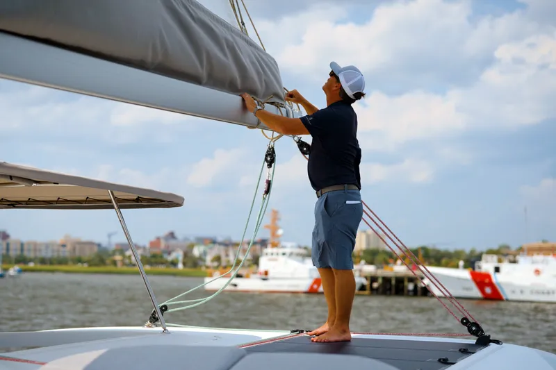 Slide: The Image of Man adjusting sail on 2026 Lagoon 38 catamaran, docked near city waterfront. - 141