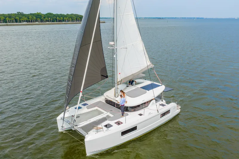 The Image of 2026 Lagoon 38 catamaran sailing on a calm lake with lush green shoreline. - 0