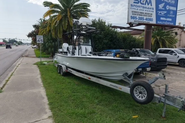 Slide: The Image of 2023 Canyon Bay 28h boat on trailer, parked roadside near palm trees and signage. - 2