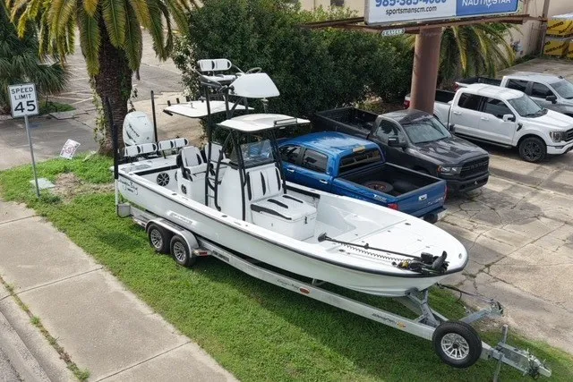 Slide: The Image of 2023 Canyon Bay 28h boat on trailer, parked near trucks, palm trees in background. - 7