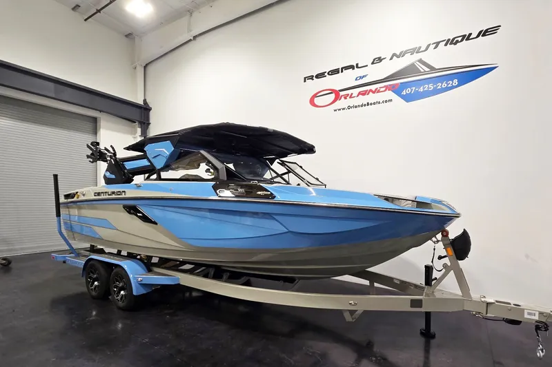 Slide: The Image of 2026 Centurion Ri230 boat in showroom, blue and gray design, on trailer. - 2