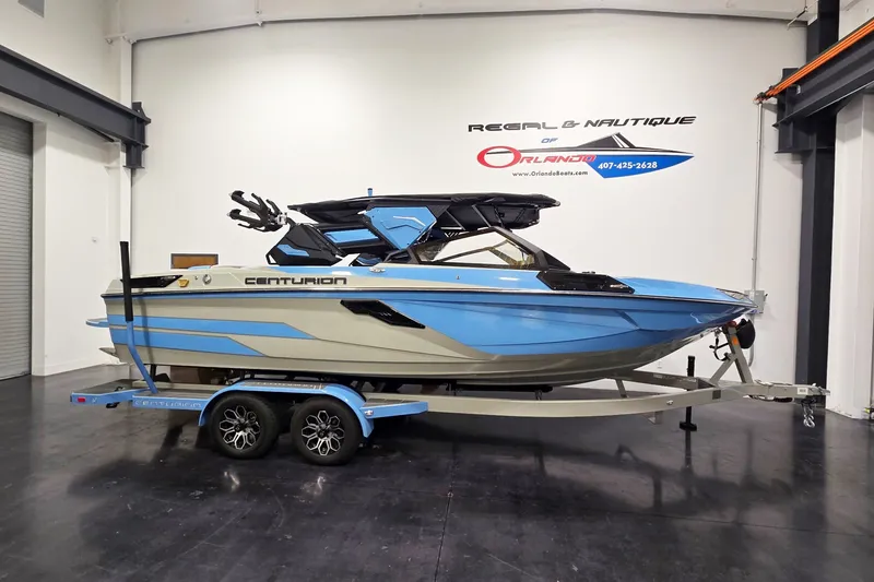 The Image of 2026 Centurion Ri230 boat in showroom, blue and white design on trailer. - 1
