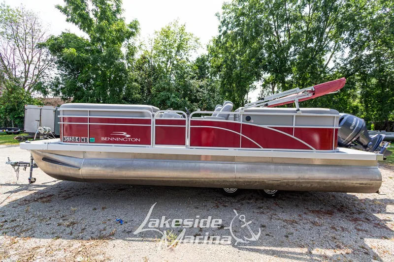 Slide: The Image of 2021 Bennington SV 22 Quad Bench pontoon boat on trailer, surrounded by trees. - 8