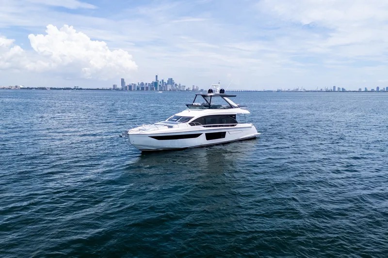Slide: The Image of 2023 Azimut Fly 68 yacht cruising on open water with city skyline backdrop. - 100