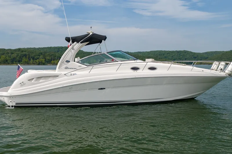 The Image of 2004 Sea Ray 340 Sundancer yacht on a serene lake with lush green shoreline. - 1