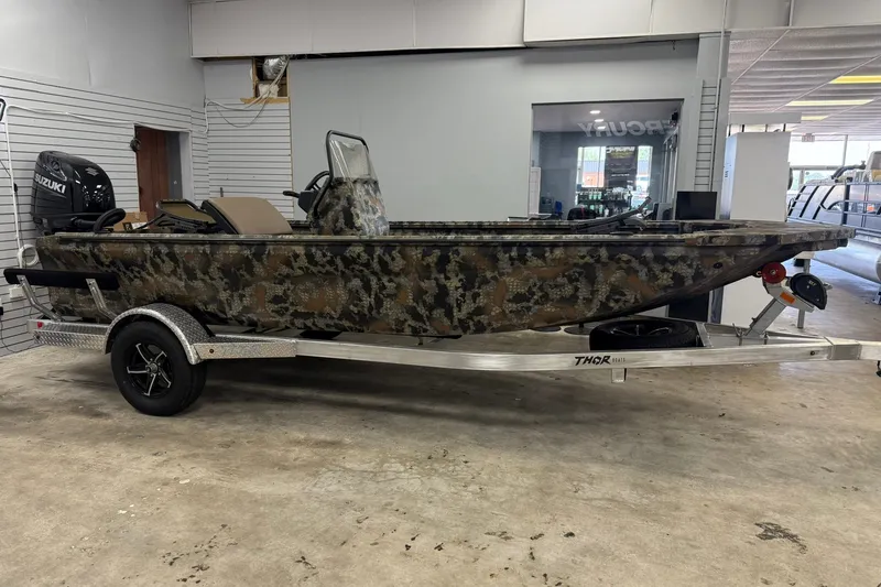 Slide: The Image of 2027 Thor BH1900CC camo boat on trailer in showroom with Suzuki outboard motor. - 2