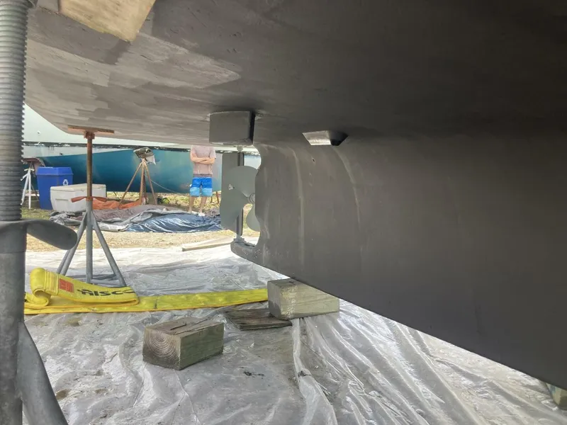 Slide: The Image of A boat hull in a shipyard, supported by wooden blocks and stands, with a visible propeller. - 32