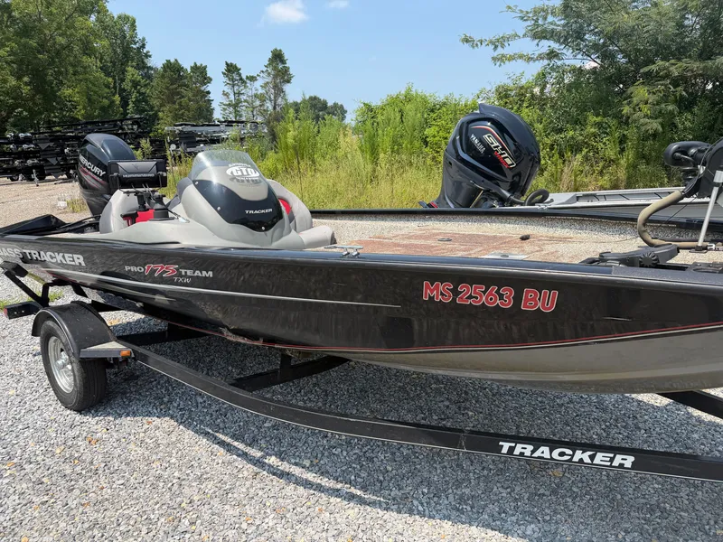 The Image of A black Tracker boat, model Pro Team 175 TXW from 2015, sits on a trailer in a gravel lot. - 1