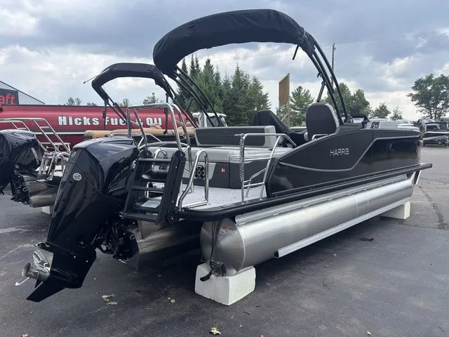 Slide: The Image of A modern pontoon boat with a black hull and two bimini tops, parked on a lot. - 6