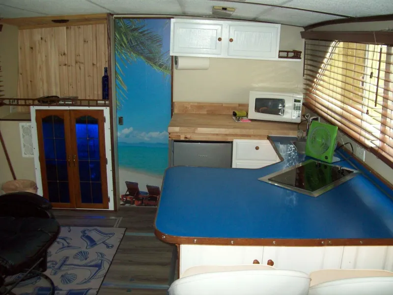 Slide: The Image of The interior of a 1979 Chris-Craft 350 Catalina features a kitchen with blue countertop, microwave, and beach image. - 6
