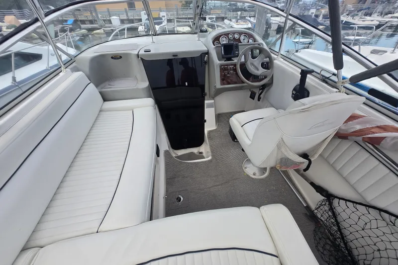 Slide: The Image of 1998 Bayliner 2655 Ciera boat interior with white seating and steering wheel, docked at marina. - 2