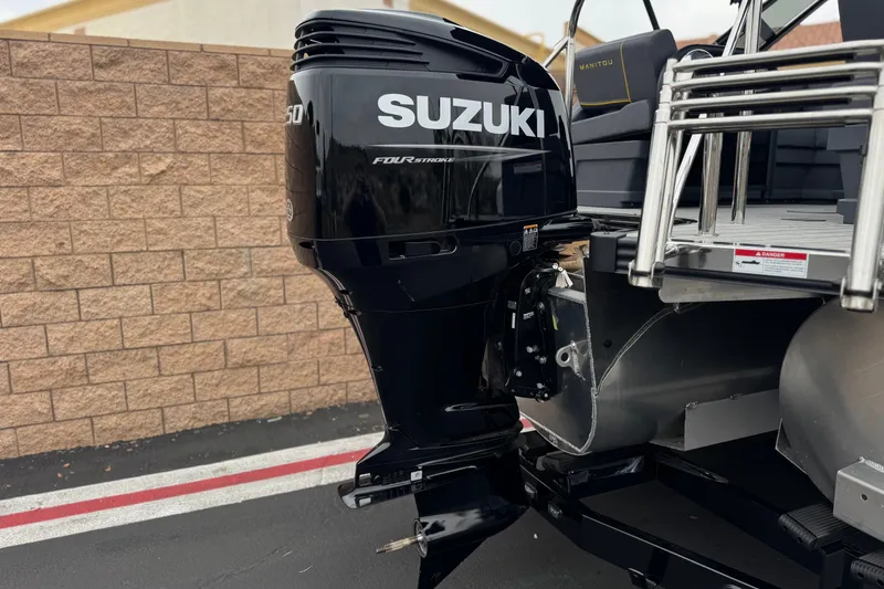 Slide: The Image of 2025 Manitou EXPLORE 24 with Suzuki outboard motor, parked near a brick wall. - 7