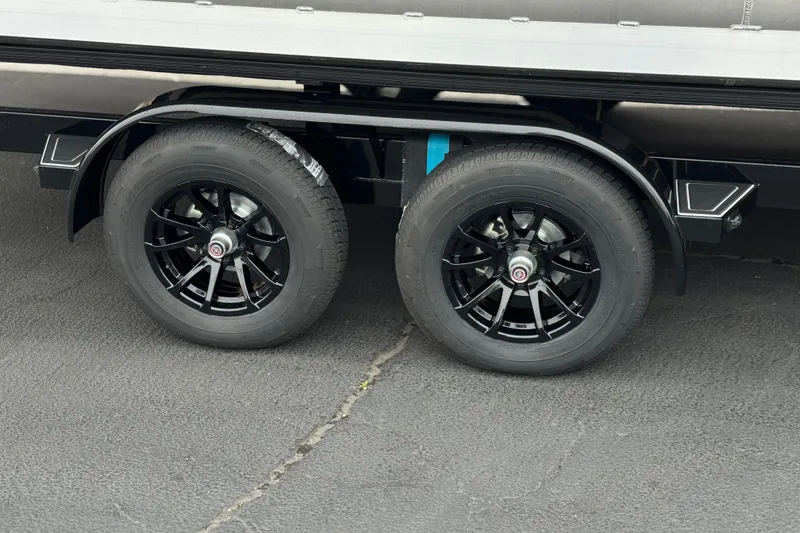 Slide: The Image of 2025 Manitou EXPLORE 24 trailer wheels on asphalt, featuring sleek black rims. - 27