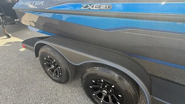 Slide: The Image of Close-up of a blue Skeeter ZXE21 boat trailer with black wheels on asphalt. - 2