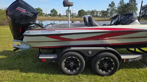 Slide: The Image of A 2021 Triton 20 TrX boat on a trailer on grass. It features red accents. - 2