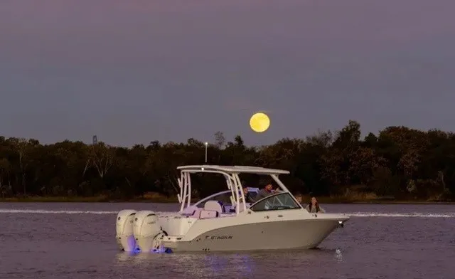 The Image of A Stingray 259 DC boat cruises on calm waters at sunset, with a full moon in the background. - 1