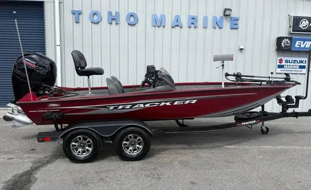 The Image of A red Tracker boat, model Pro Team 195 TXW Tournament Edition, sits on a trailer outside a building. - 1