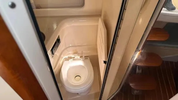 Slide: The Image of The image shows a compact boat toilet with a white toilet and wooden flooring. - 16