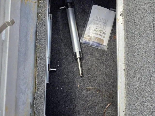 Slide: The Image of An open storage compartment with a metal cylinder and a manual on gray carpeted flooring. - 23