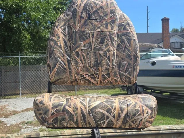 Slide: The Image of A boat seat with camouflage pattern, outdoors next to a fence and another boat. - 15