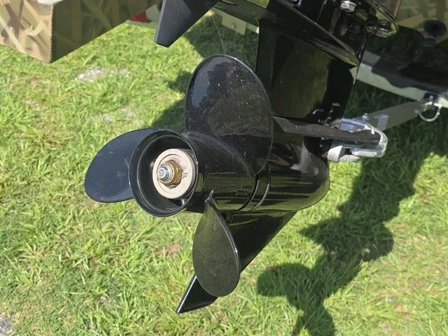Slide: The Image of A black boat propeller on green grass. It has four blades and is shiny. - 25