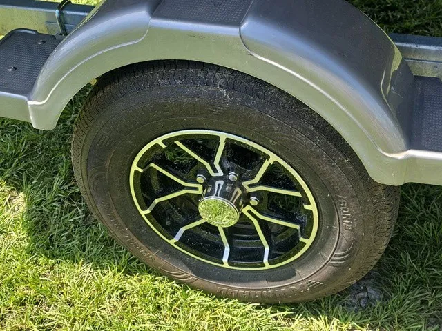 Slide: The Image of A boat trailer wheel with a black rim and yellow accents on grass. - 22