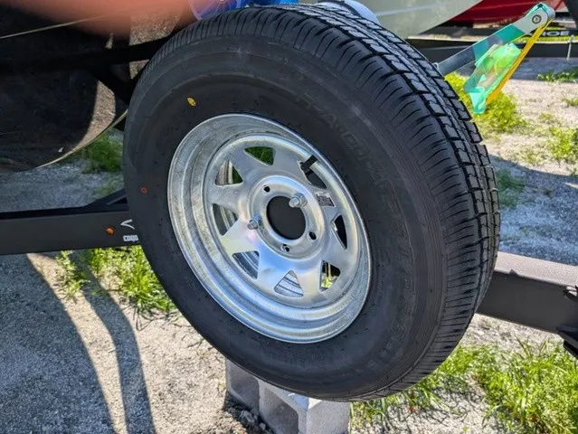Slide: The Image of A trailer tire with a silver rim, parked on gravel, surrounded by grass. - 4
