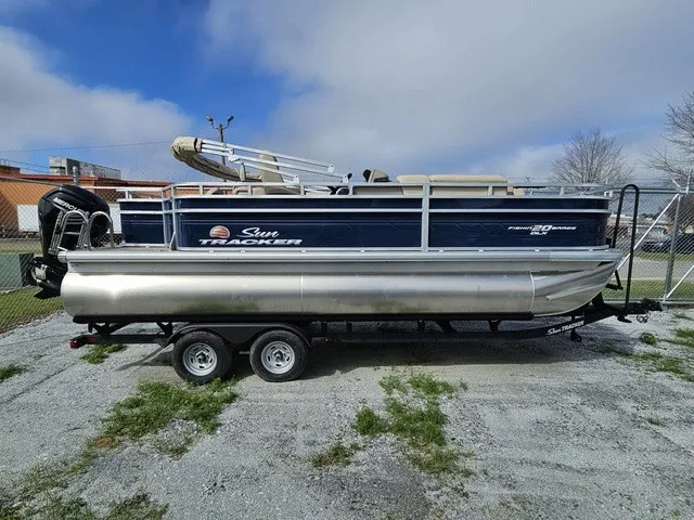 Slide: The Image of A 2025 Sun Tracker Fishin' Barge 20 DLX pontoon boat on a trailer in a gravel lot. - 3