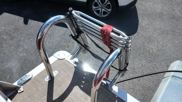 Slide: The Image of A foldable stainless steel swim ladder on a boat, secured with a red strap. - 22