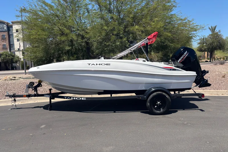 The Image of 2027 Tahoe T16 boat on trailer, parked outdoors, featuring sleek white design and Mercury outboard motor. - 0