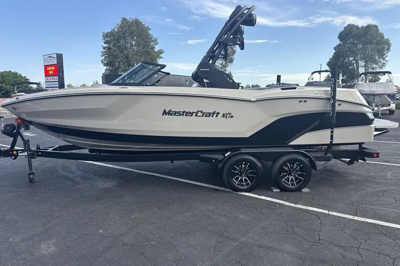 Slide: The Image of A 2027 MasterCraft NXT23 boat on a trailer in a parking lot. - 2