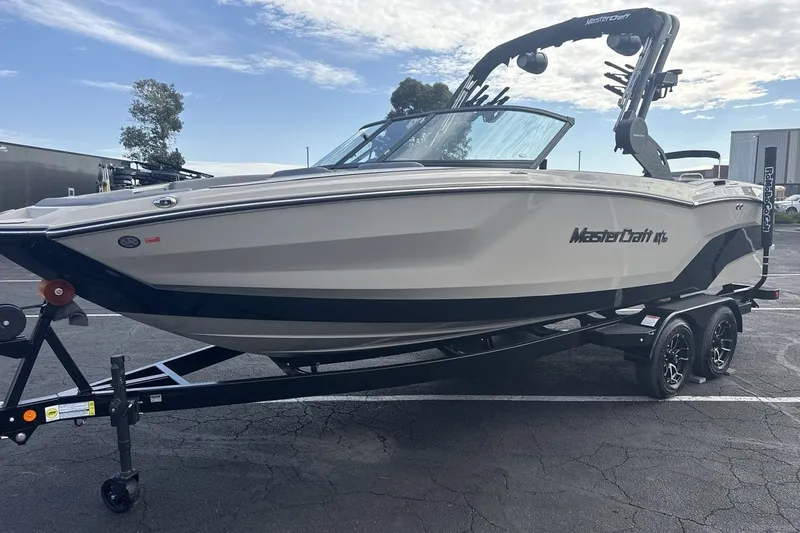 The Image of A white 2027 MasterCraft NXT23 boat on a trailer in a parking lot. - 1