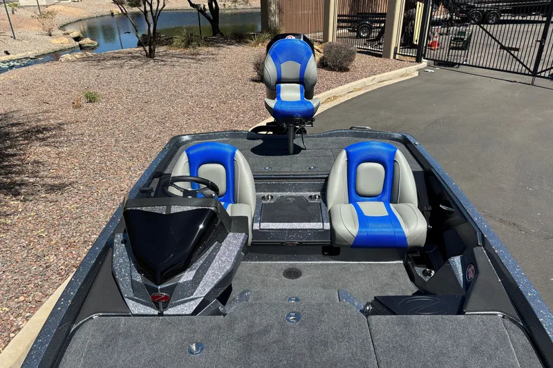 Slide: The Image of 2027 Ranger Z518 Cup-Equipped boat with blue and gray seating, parked near a pond. - 17