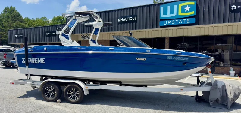 Slide: The Image of A blue and white motorboat, Supreme S220 model from 2022, on a trailer in front of a building. - 2