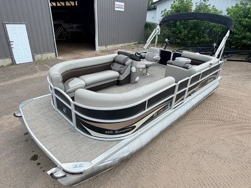 The Image of A 2016 Premier 220 SunSpree pontoon boat with a 50HP Honda 4-stroke engine, parked in a yard. - 1