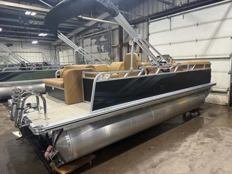 Slide: The Image of A modern pontoon boat with a black hull and beige interior sits in a warehouse. - 40