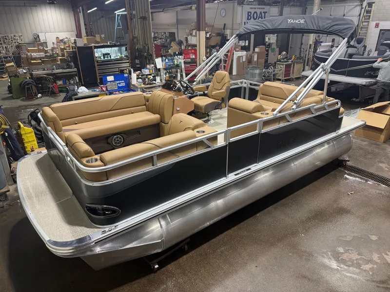 The Image of A modern pontoon boat with beige seating and a black hull in a workshop setting. - 1