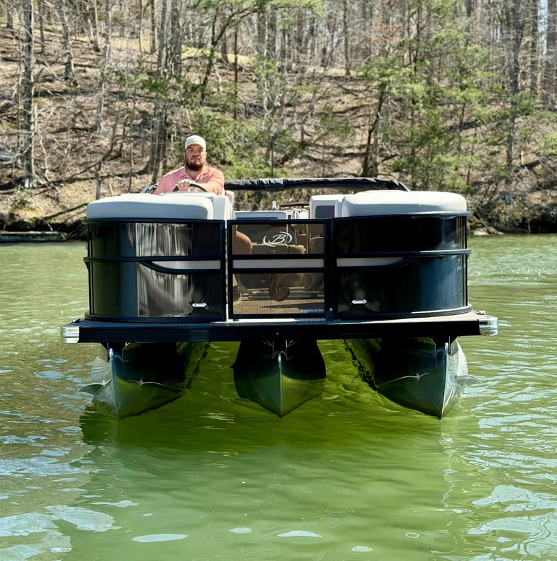 Slide: The Image of A man navigates a Barletta Cabrio 24 UE pontoon boat on a calm lake. - 18