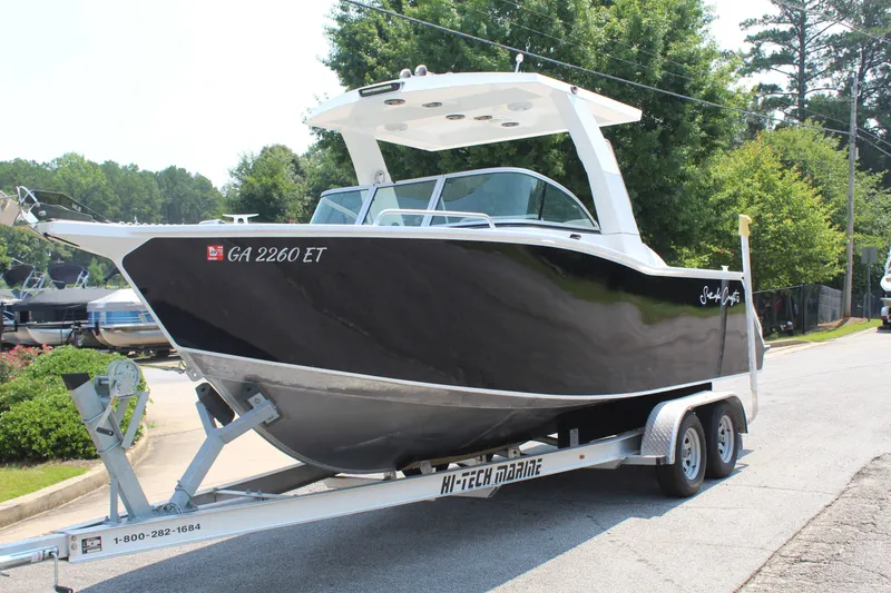 Slide: The Image of A black boat on a trailer with a white roof and windshield, parked on a street. - 2