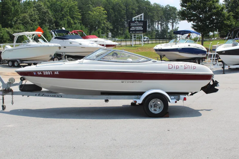 The Image of A white and red 2012 Stingray 185 LS boat on a trailer in a parking lot. - 1