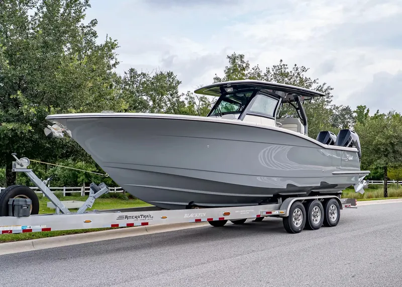 The Image of A 2027 Scout 330 LXF boat on a trailer, surrounded by trees and a road. - 1