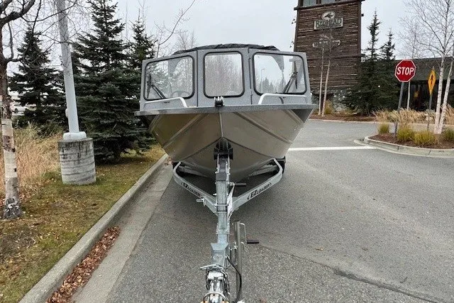 Slide: The Image of 2024 Spartan 185 Astoria boat on trailer, parked on a street near trees and a building. - 2