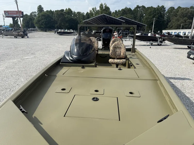 Slide: The Image of An olive-green boat with two seats and a helm, surrounded by other boats on a gravel lot. - 3