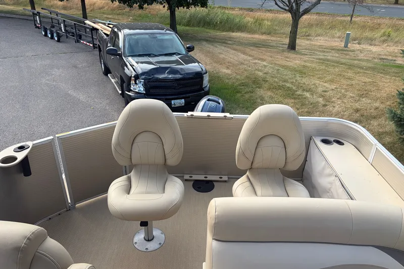 Slide: The Image of 2015 Sweetwater 2286 pontoon boat interior with beige seating, parked near a black truck. - 12