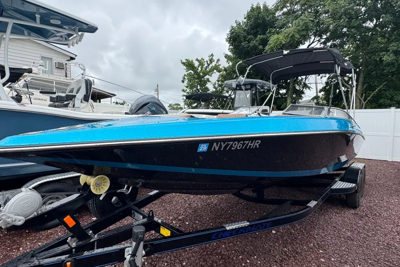 Slide: The Image of 2021 Checkmate Pulsare 2400 BRX boat on trailer, blue and black design, parked outdoors. - 6