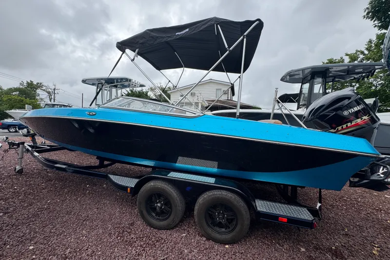 Slide: The Image of 2021 Checkmate Pulsare 2400 BRX boat with blue and black design on a trailer. - 5